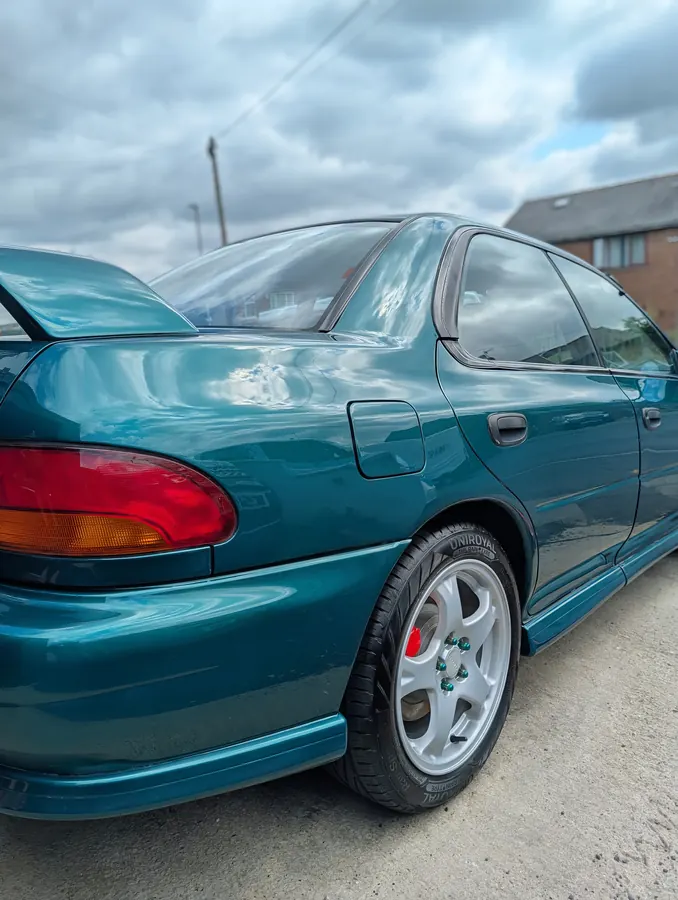 Rear of a green Subaru Impreza with sky reflected in the paint